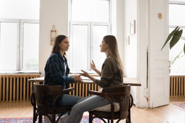 İşbirlikçi tartışma. İki genç bayan iş arkadaşı çalışma masasında oturup sohbet ediyorlar. Pazarlama stratejisi üzerine fikir alışverişi yapıyorlar. Proje planlarını birlikte tartışıyorlar.