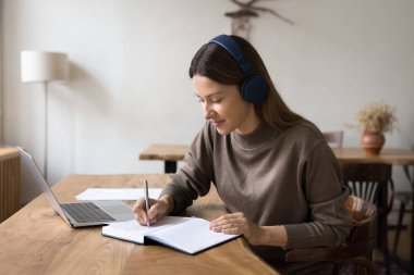 Modern zaman uzaktan öğrenicisi. Dijital kulaklıkla gülümseyen genç kız lise öğrencisi ev izleyip bilgisayarla melez eğitim platformu hakkında sanal e-öğrenme dersi alıyor.