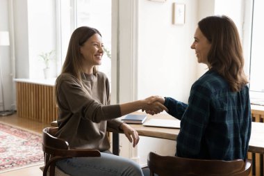 Verimli işbirliği. Mutlu gülümseyen genç iş kadınları iş arkadaşları ofis masasıyla tokalaşıyor yaratıcı proje üzerinde uzlaşmaya varılmasından memnun oluyorlar. Fikirleri sonuçlandırmak başarılı bir anlaşma sağlıyor.