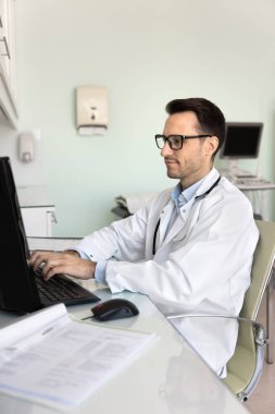 Muayene evraklarını gönder. Erkek doktor sağlık uzmanı hastane vardiyasında idari işler yapıyor klinikte bilgisayar kullanıyor hasta geçmişi ile ilgili tıbbi belgeler hazırlıyor