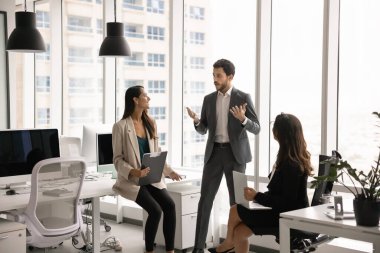 İş ekibi, kısa günlük toplantılarda takım çalışması ve planlama görevlerini tartışıyor. Proje yöneticisi, çeşitli meslektaşlarına talimat veriyor, güncellemeler yapıyor. Daire halinde oturuyor ve ofis çalışma alanını konuşuyor.