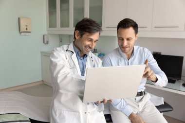 Dostça bir tanı tartışması. Gülümseyen erkek doktor pratisyen hekimi, sağlık bilgilerini ilgili hastaya not ekranında açıklıyor. Tedavi planını tartışıyor, tıbbi sonuçları görsel veri kullanarak yorumluyor.