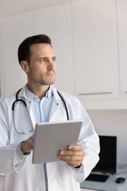 Tıpta eleştirel düşünce. Tıp bürosunda tablet kullanan ciddi profesyonel doktor. Ekranı bir kenara bırak. Hasta teşhisi üzerinde kafa yorma seçenekleri değerlendirme ameliyat riskini göz önünde bulundur.