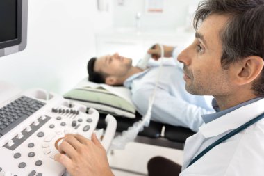Sonolog iş başında. Portreyi kapat. Ciddi erkek doktor radyoloji uzmanı. Tıbbi görüntüleme uzmanı. Kanepede yatan hastayı kontrol paneli ve sensör izleme ile muayene ediyor.