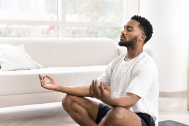 Huzurlu meditasyon ve farkındalık. Sakin genç sporcu yerde bacak bacak üstüne atarak oturur derin gözleri ile derin derin Mudra jestleri ile ellerini meditasyon yapar vücut zihninin iç dengesine ulaşmak için. Boşluğu kopyala