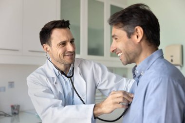 Sağlıklı kalp muayenesi. Kendine güvenen erkek doktor kardiyolog klinikteki rutin muayene sırasında orta yaşlı bir hastanın kalp atışlarını kontrol etmek için steteskop kullanır.