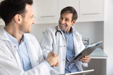 Karşılıklı saygı ve işbirliği. Mutlu gülümseyen erkek doktor, beyaz önlüklü meslektaşıyla başarılı bir değerlendirmeden sonra uzman görüşleri için teşekkür ediyor.