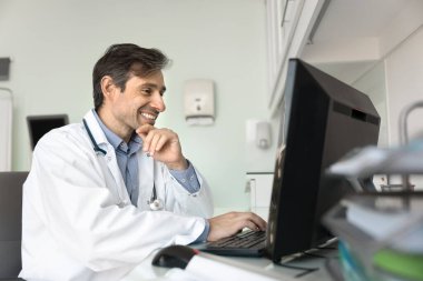 Tıbbi çalışmada motivasyon. Klinikte bilgisayar üzerinde çalışan mutlu gülümseyen erkek doktor başarılı sağlık projesi güncellemesi hastadan gelen minnettar mesajı okuyun ve test sonuçlarında olumlu ilerleme görün