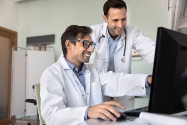 Hastane çalışmalarında takım ruhu. Mutlu gülümseyen erkek doktorlar ameliyat sonuçlarını tartışmak için masaüstü bilgisayarlarını kullanırlar terapi sürecini paylaşırlar tıbbi araştırma bilgilerini hevesle incelerler.