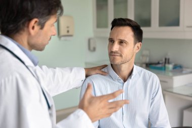 Doktoruma güveniyorum. Dikkatle odaklanmış orta yaşlı erkek hasta klinikteki doktor cerrahı dinle. Omzuna dokunan şefkatli doktordan tavsiye al.