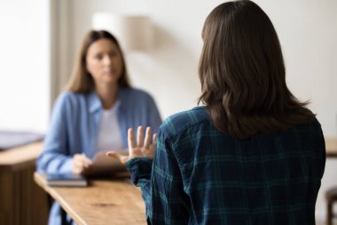 Kendini tanıtıyor. Arkadan bakan genç bayan başvuru sahibi, işe alım görüşmesi sırasında işe alım için kağıt özgeçmişiyle masada oturan işe alım görevlisi bayan işverenle gündelik bir konuşma yapar.