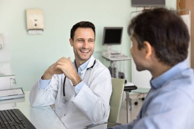 Hastanın güvenini kazanmak. Dost canlısı, destekleyici orta yaşlı doktor terapisti klinikteki masada oturup erkek müşteriyle rahat rahat sohbet eder ve tedavi sürecini tartışır.