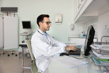 Tıbbi kayıt tutuyorum. Klinik ofisindeki masaüstü bilgisayarında çalışan orta yaşlı erkek doktor GP hemşiresi hasta dosyalarını randevu saatinden sonra çevrimiçi formlara girin