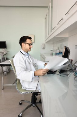 Tıptaki veri yönetimi. Laboratuvar önlüklü erkek tıp uzmanı. Hemşire hastane ofisinde günlük evrak işleriyle uğraşıyor. Hasta bilgilerini gözden geçirmek için bilgisayar kağıdı kullanıyor.