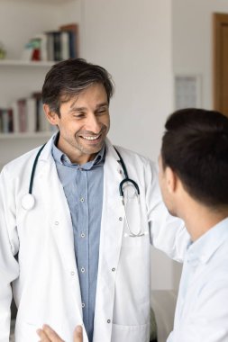 Klinik pratikte olumlu iletişim. Dikey çekim gülümseyen erkek doktor uzman doktor hastayı sıcak jest konuşmalarıyla cesaretlendiriyor.