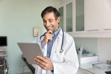 Tıbbi araç olarak dijital teknoloji. Gülümseyen olgun erkek doktor aile terapisti tablet bilgisayar ekranına bak. Hasta tanıları üzerinde düşün. Dosyaları oku.