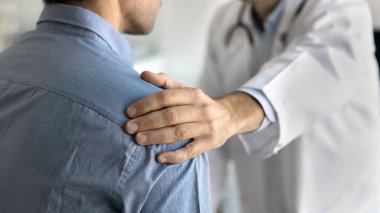 Bir doktorun güven verici dokunuşu. Yakın çekim, şefkatli tıbbi uzman erkek hastanın omuz omuza ilgilenmesi. Hastalık konseptini aşan teşhisi kabul etmede duygusal destek