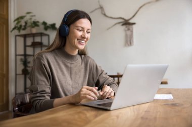 Sanal öğrenme. Neşeli genç kız uzaktan kumandalı öğrenci, bilgisayar aracılığıyla öğretmenle melez iletişimi sağlayan bir ekran aracılığıyla rahat çalışma masasında dijital kulaklık takıyor.