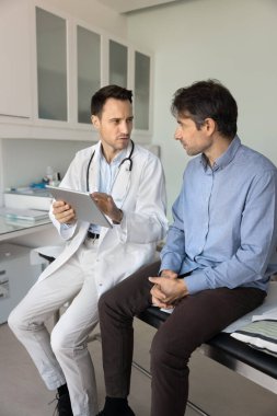 Tıbbi bilgileri paylaşıyoruz. Klinikteki orta yaşlı erkek hastaya pratisyen hekimlik konusunda uzman. Ameliyat detaylarını tablet reçeteli ilaç kullanarak açıkla.