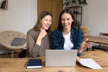 Dostça işbirliği ve ortaklık. 2 mutlu genç bayan ofis çalışanı masamda rahat stüdyo çalışma alanındaki dizüstü bilgisayarın başında oturmuş ilerleme kaydetmekten heyecan duyan yaratıcı fikirleri paylaşarak gülüyorlar.