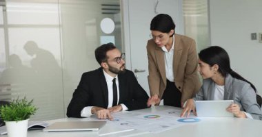 İki yöneticinin kağıt pazarlama raporlarını inceleyen mutlu iş geliştirme danışmanı. Üç iş arkadaşından oluşan bir ekip finansal istatistik tablolarını tartışıyor, toplantı masasında satışların artışı...