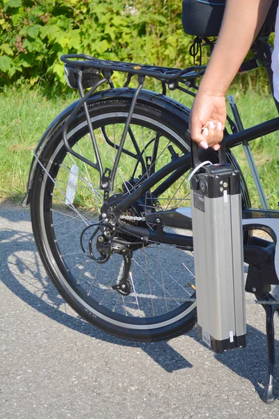 Women holding battery pack of electric bicycle near her e bike. On the background is e bike back wheel with electro motor and gear.  Ecology concept.