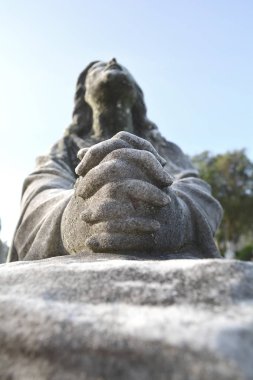 Scene of Jesus Christ praying to God, his Father. Statue or sculpture of Jesus looking up to the blue sky. Focus on the praying hands.  clipart
