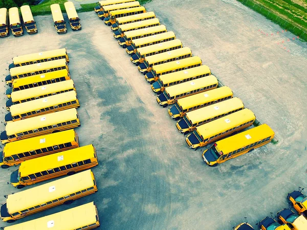 School bus vehicles ready for school educational season. Drone aerial view of parking yard with yellow tracks and evening sky ready to pick up and drop off young college students. Back to school idea.