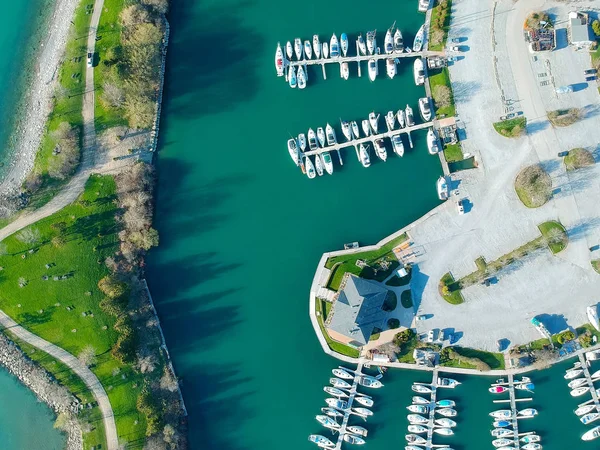 Aerial view of sailing yachts and boats near wooden piers. Top view of American city large boat parking near sea coast. Island and parks with green grass. Beginning of summer concept.