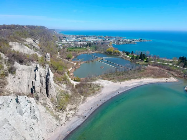 A beautiful sunny day aerial bluffs beach view below with people. Bird eye view of cliffs formed by lime stones along the lake above the water. Sandy beach with green water below.