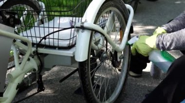 Sarı eldivenli bisikletçi yaz günü dışarıda elektrikli bisikletarka tekerleği temizliyor. Binici e bisiklet tekerleği dikkat çekmek. Güç pili ve kumanda dişlisi çerçevededir. 4k