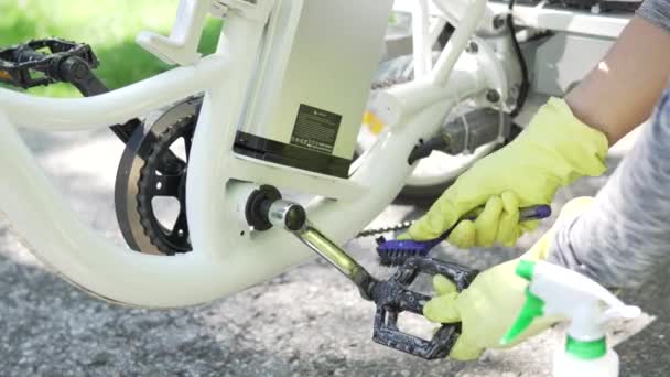 Cyclist in yellow gloves is water spray cleaning pedal of the electric bicycle outside in the summer day. Part of the power battery in the frame. Rider take care of the sport e bike. 4k — Stock Video