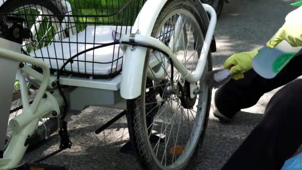 Cyklist i gula handskar är rengöring av elektrisk cykel bakhjulet utanför på sommardagen. Rider ta hand om e cykelhjulet. Ström batteri och Controller redskap är i ramen. 4K — Stockvideo