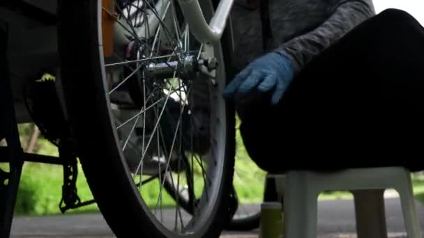 Cycliste en gants de caoutchouc bleu nettoie la roue arrière du vélo électrique à l'extérieur dans la journée d'été. Mouvement motorisé lent de tir de poupée, mouvement latéral de camionnage de curseur de gros plan d'en bas. 4k — Video