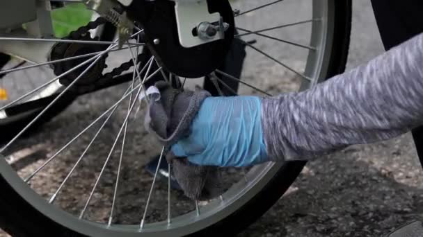 El ciclista con guantes de goma azul está limpiando la rueda trasera de la bicicleta eléctrica en el día de verano. Movimiento de disparo de dolly motorizado lento, movimiento lateral de camiones deslizante de cerca desde abajo. 4k — Vídeo de stock