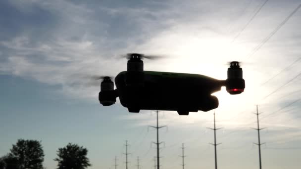 Sílhueta de drones a voar ao nascer do sol. Os raios solares saem do avião em forma de drone levitando estacionário. Conceito de tiro no hobby aéreo. 4k . — Vídeo de Stock