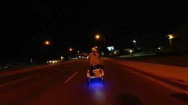 Mezrada kadın gece üç tekerlekli elektrikli bisiklet ihya, arkadan görünümü. Bisikletçi banliyö trafik ışıkları, arabalar ve evler ile şehir yolunda e bisiklet sürme. 4k ebike aksiyon kamerası.