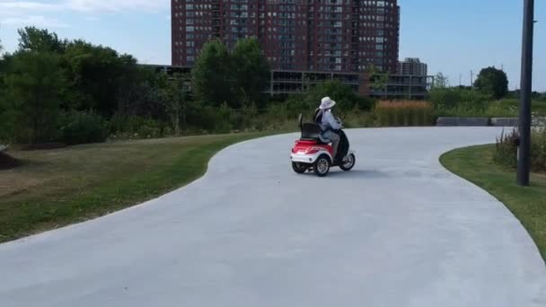 サングラスと帽子に乗って電動スクーターに乗ってアフリカ系アメリカ人の女性 夏の日に緑の都市公園に沿ってモビリティ車両に乗るの自由 — ストック動画