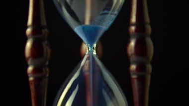 Dönen kum saati saat saati kavramı. Video açma kum saati sonunda sona eriyor. Eski vintage ahşap çerçeve mavi kum saat yavaş yavaş koyu arka plan üzerinde dönen. Yakın çekim.