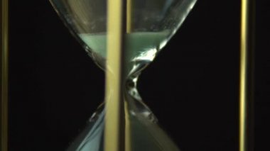 Kum zamanlayıcı saatinin saat camından akan kumla yavaş hareket döndürmesi. Kum saati makro çekimi kapatın. Siyah arka plan