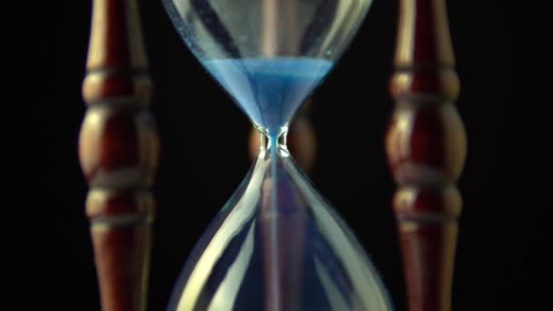 時計の時間の概念を回転させる ビデオオープニングサンド時間は 最後に終了します 古いヴィンテージウッドフレーム青い砂時計は 暗い背景にゆっくりと回転します クローズアップ — ストック動画