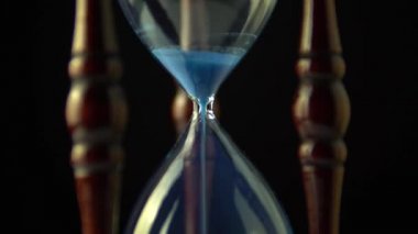 Dönen kum saati saat saati kavramı. Video açma kum saati sonunda sona eriyor. Eski vintage ahşap çerçeve mavi kum saat yavaş yavaş koyu arka plan üzerinde dönen. Yakın çekim.