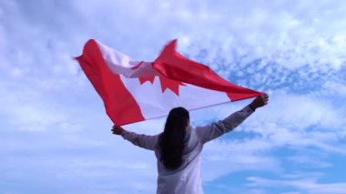 Neşeli Kanadalı kadın, elinde Kanada bayrağı sallayarak gecenin altın saatinde ayakta duruyor. Neşeli yetişkin vatandaş siyah kadın gururlu ve elinde kırmızı akçaağaç yaprağıyla ulusal bayrak tutuyor..