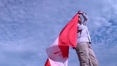 Kanadalı bayrağı rüzgarda tutan Afro-Amerikalı kadının portresi. Güneşe ve mavi bulutlu gökyüzüne bakıyor. Mutlu Kanada vatandaşları. Vatanseverlik kavramı.