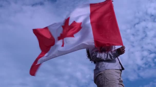 Mulher adulta de pé com orgulho e bandeira canadense acenando. Símbolo Canadá. Mulher negra orgulhosa e segurando bandeira nacional com folha de bordo vermelho em pé sozinho no fundo do céu azul. Conceito de patriotismo ., — Vídeo de Stock