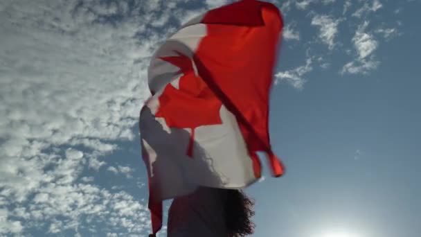 Canadese vrouw met een Canadese vlag met rood esdoornblad tegen de wind in met het gevoel van trots. Gouden uur avond, zonsondergang. Bijna silhouet bliksem en haar gezicht schaduw op de vlag. — Stockvideo