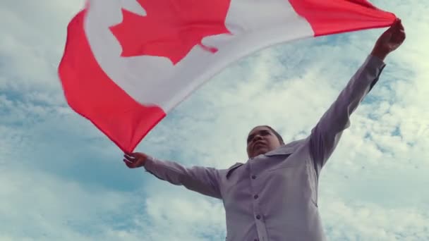 Portrait from the side of African American woman holding Canadian flag at wind and looking at sun and blue cloudy sky. Happy Canada citizen. Patriot concept. — Stock Video