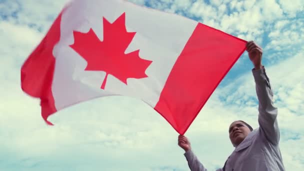 Joven mujer afroamericana adulta con la bandera canadiense lo mira y sonríe. Patriota ciudadano y celebración del Día de Canadá 1 de julio concepto. Vista desde abajo . — Vídeos de Stock