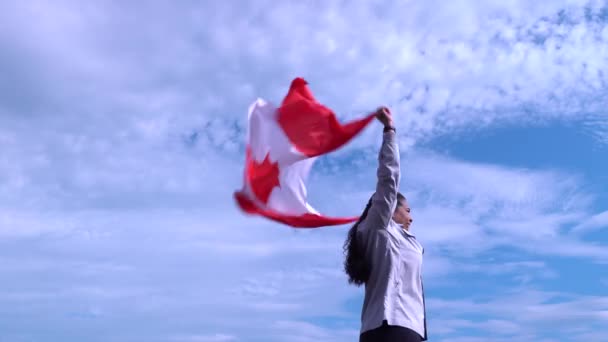 Канадка махає прапором Канади, стрибаючи і посміхаючись. Канадська шанувальниця тримає національний прапор і пишається ним. Приваблива концепція. — стокове відео