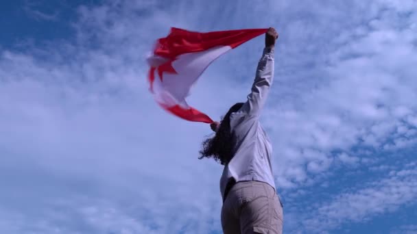 Mulher adulta de pé com orgulho e bandeira canadense acenando. Símbolo Canadá. Mulher negra orgulhosa e segurando bandeira nacional com folha de bordo vermelho em pé sozinho no fundo do céu azul. Conceito de patriotismo ., — Vídeo de Stock